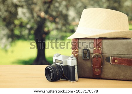 traveler vintage luggage, camera and fedora hat over wooden table infront of bokeh landscape. holiday and vacation concept
