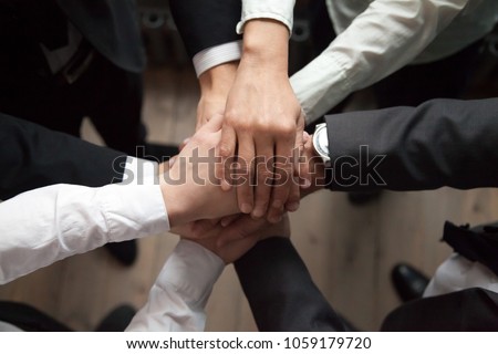 Motivated business people put hands together, sales team engaging in teambuilding activity promising help in collaboration, commitment in teamwork, unity trust and support concept, close up top view Royalty-Free Stock Photo #1059179720