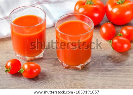 Fresh tomato juice in two glass cups and tomatoes on a closeup table.