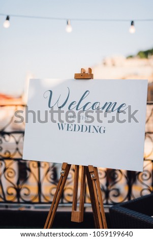Easel with white board with lettering 'Welcome to the wedding' stands on the balcony