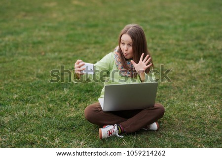 Pretty female in trendy outfit resting during free time taking photo on smartphone camera and using laptop on grass.