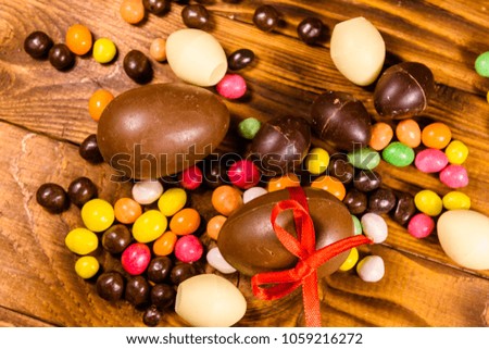 Chocolate easter eggs and multicolored candies on rustic wooden table. Top view