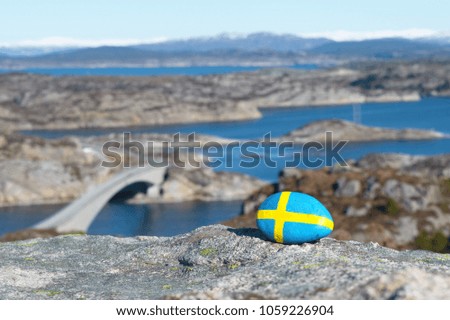 at the top of the hill a stone with a picture of a Sweden flag against a background of the sea coast