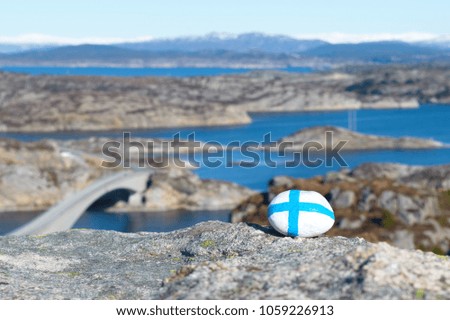 at the top of the hill a stone with a picture of Finland flag against a background of the sea coast