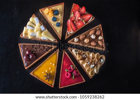 Dessert table is a tart cake with different fillings of fruits, berries, nuts and chocolate close-up. Fresh food cake on a dark background top view. Royalty-Free Stock Photo #1059238262
