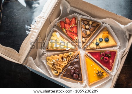 Present in the box - tart cake with different fillings of fruits, berries, nuts and chocolate close-up. Fresh food cake on a dark background top view. Royalty-Free Stock Photo #1059238289