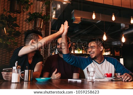 Happy arabic young man giving high five to his friend. Group of mixed race people having fun in lounge bar