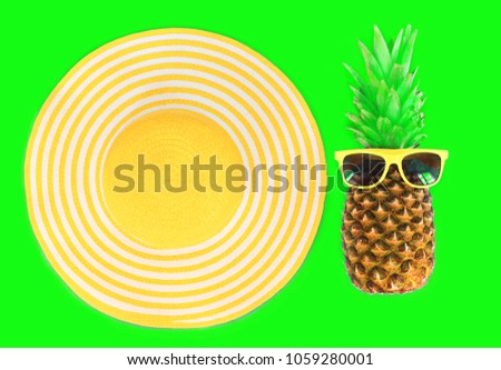 Pineapple with sunglasses and yellow straw beach hat on green background top view