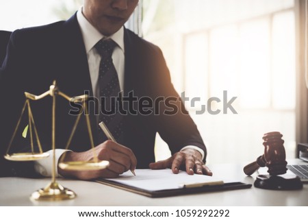 Lawyer in the office with brass scale and writing in contract on wooden table. Justice and law concept. Royalty-Free Stock Photo #1059292292