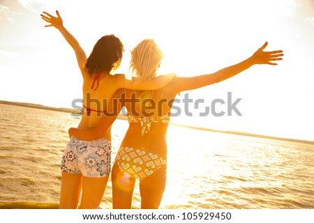 two beautiful young girlfriends opened her hands with delight at the blue sea and sky