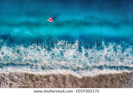 Aerial view of young woman swimming on the pink swim ring in the transparent turquoise sea in Oludeniz.Top view from drone