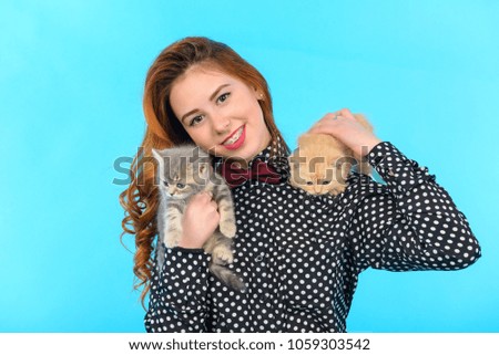 young girl with long hair and in fashion clothes lies on a blue background and holds two cats