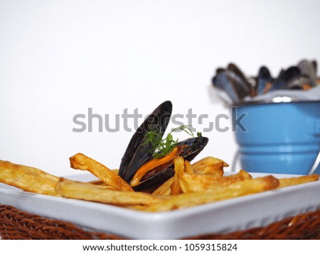 A cooked mussel on top of homemade golden french fries, a blue bucket of mussels in background