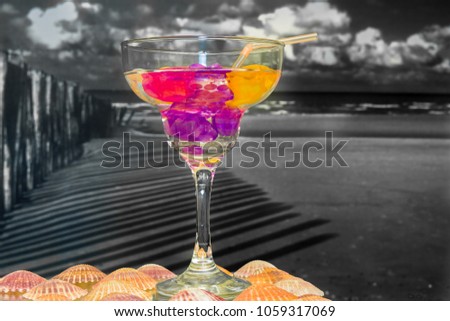 Picture of drink glass with colorful content and colorful straw  against black and white beach backgroung 