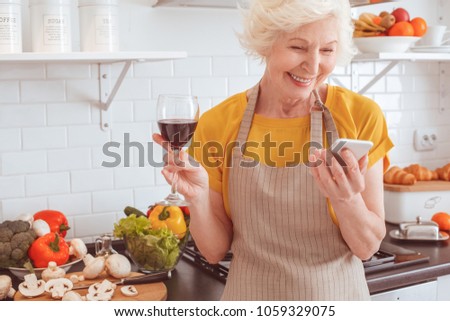 Grandmother drinks wine and looks at the pictures of mobile