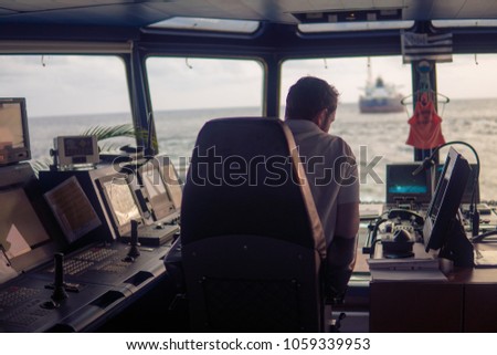 Deck navigation officer on the navigation bridge. He looks at radar screen. Watchkeeping, collision prevention at sea. COLREG Royalty-Free Stock Photo #1059339953