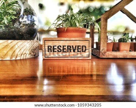 Reserved wooden signage placed on the wood table for receptionist & reservation team in restaurant, café, coffee shop, meeting room with  many trees on the flower pots and blurred background bokeh.