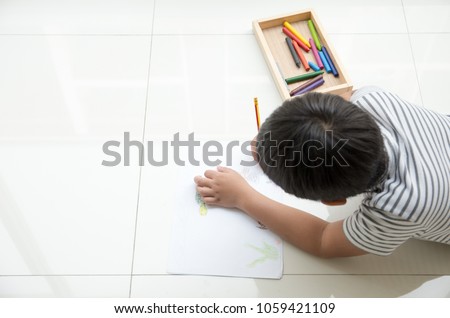 Happy Asian kid lying down on the floor and enjoy drawing animal cartoon