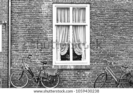 White window with Curtain and retro bicycles in the Dutch City. Bikes leaning against the red brick wall in Amersfoort. Black and white picture