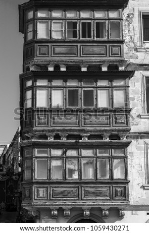 Building with traditional colorful maltese balcony in historical part of Valletta. Windows on the facade of a house in Malta. Black and white picture