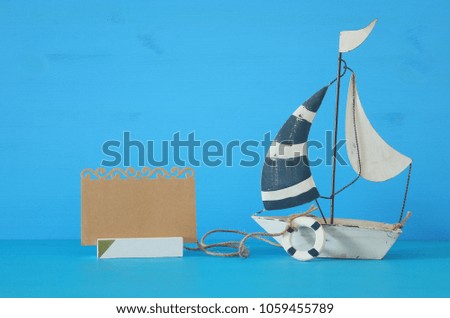 nautical concept image with sail boat and empty note over blue wooden table and background
