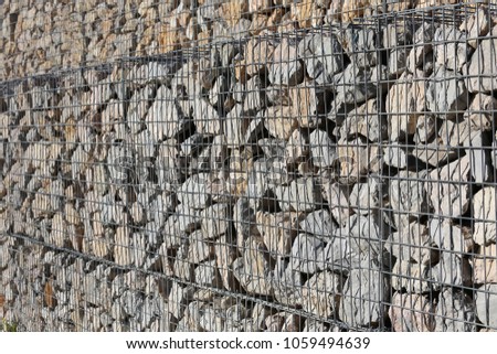 Close up outdoor view of a stone protection wall made of gabions. Pattern of rocks put into iron wires cages. Geometric design of a building structure. Rough grey brown surface. Abstract urban image  