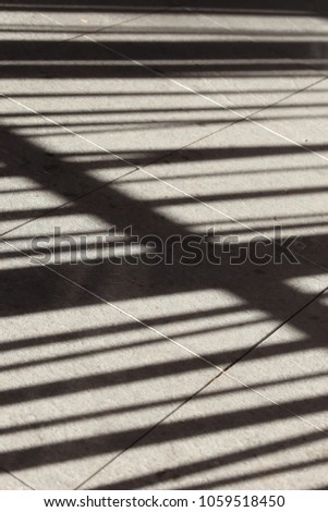 Close up perspective view of the shadow of a metallic railing gate drawn on the floor. Pattern of dark leading lines and bars. Geometric abstract design. Fence silhouette projected on the ground. 