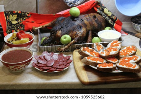 Chic still life with baked goose decorated with green apples, also sandwiches with butter and red caviar. Cozy and tasty homemade food. Appetizing and useful gala dinner
