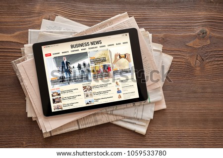 Tablet with business news website on stack of newspapers. All contents are made up.