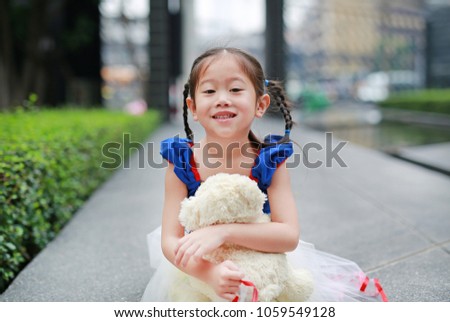 Smiling little asian girl dressed with a fantasy costume sitting in the garden with teddy bear.