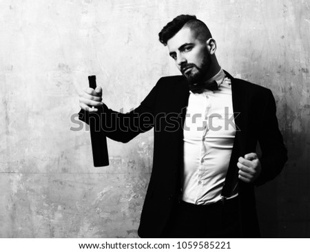 Guy with beard in elegant suit and bottle of wine in hand, on beige background. Concept of celebration and party