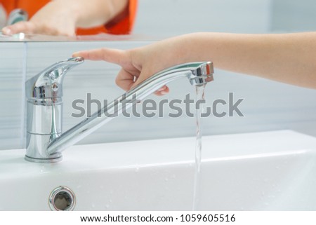The child's hand closes the water from the mixer by pressing the finger on the handle Royalty-Free Stock Photo #1059605516