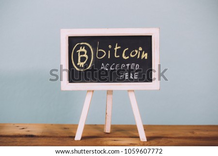 Virtual currency Bitcoin accepted here sign on wooden platform over pastel blue background