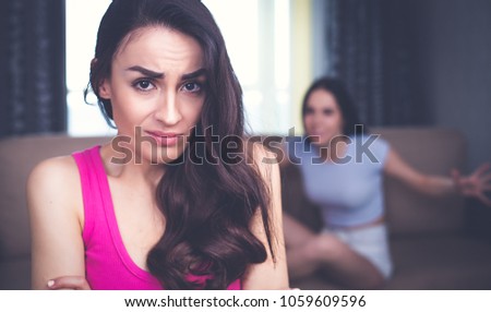 Conflicts between friends. The quarrel of two girls. In the foreground an offended and frustrated young woman looks into the camera, and against the background her friend yells at her.