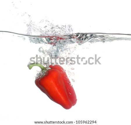 Red pepper falling into water over white background