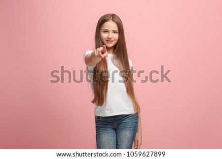 I choose you and order. The smiling teen girl pointing to camera, half length closeup portrait on pink studio background. The human emotions, facial expression concept. Front view. Trendy colors