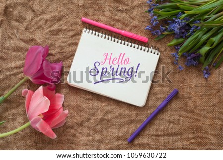 Two tulips with Scilla bifolia and blank notepad with colored pens on a sackcloth texture. Hello Spring Text Template