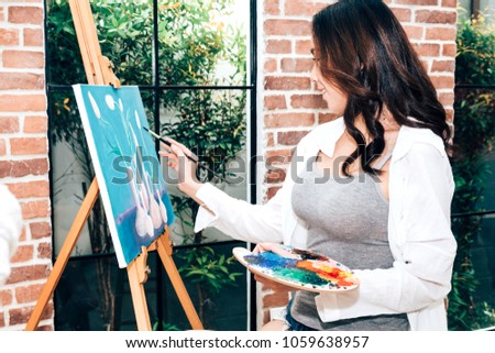 Young woman artist drawing on canvas with color palette and watercolor paints at home