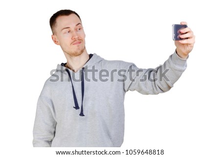 Picture of young man posing over white background and make a selfie by phone. Looking at phone.