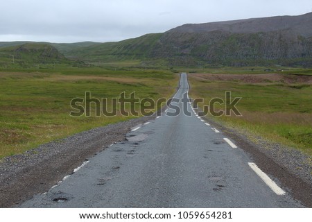 Landscape picture of a straight asphalt road stretching ahead through flat landscape on a grey day, captured on the way to Båtsfjord, Finnmark county, Norway