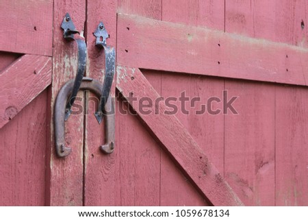 Old iron good luck horseshoe hanging on handles of weathered rustic red country barn 