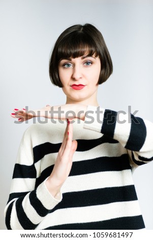beautiful young woman shows a break or a timeout, a short haircut, wears a sweater, studio photo on a background