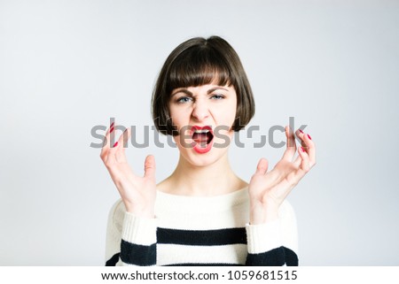 beautiful young woman angry screaming, short haircut, wearing a sweater, studio photo on the background