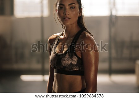 Strong and determined female in sportswear standing in the gym and looking at camera. Sportswoman after intense crossing training workout session in gym. Royalty-Free Stock Photo #1059684578