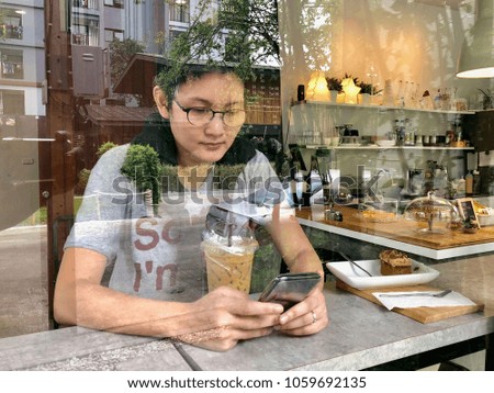 Asian beautiful woman wearing casual outfit sitting in front of coffee shop using smart phone and drink coffee