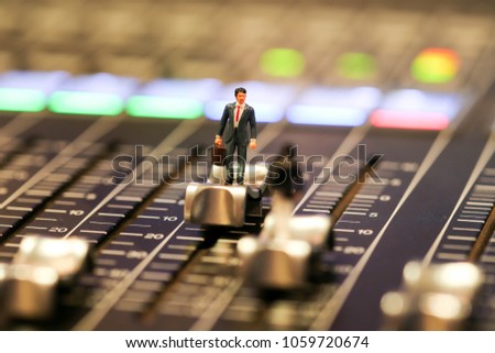 Miniature people : business man standing  on Professional audio mixing console with faders and adjusting knobs,TV equipment ,sound musical mixing&engineering concept background