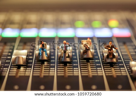 Miniature people : business man sitting on Professional audio mixing console with faders and adjusting knobs,TV equipment ,sound musical mixing&engineering concept background
