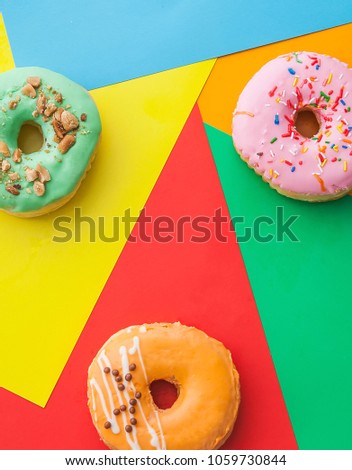 Three bright donuts on a colored background. Light green, pink and orange donations with powder and glaze.