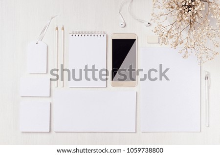 White blank stationery, flowers as work place with phone, earphone on light white wood background. Mock up for branding, graphic designers presentations and business portfolios.