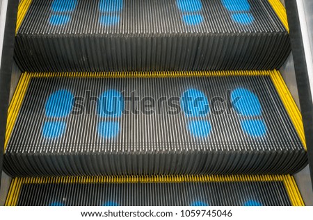 Staircase escalator in shopping mall moving up with blue footprint graphic symbol for position.